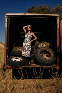 Woman in a dress standing inside an open truck with tires in a desert setting